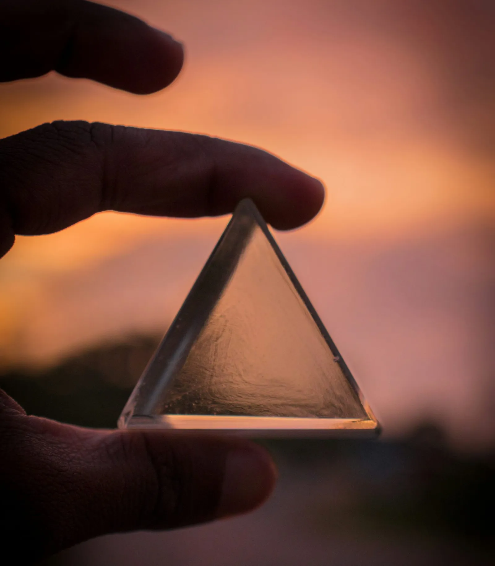 Main tenant un prisme triangulaire en verre devant un coucher de soleil