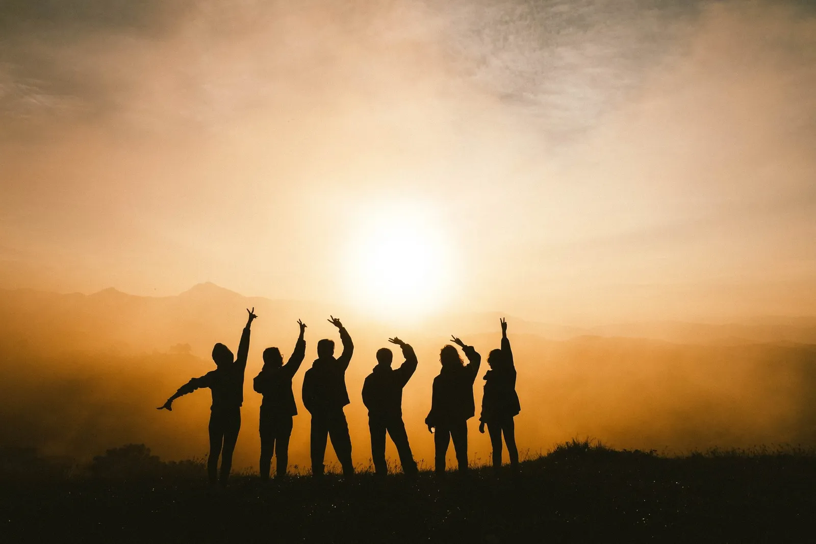 Groupe d'amis en silhouette, bras levés, face au soleil couchant